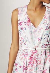 Ärmelloses V-Ausschnitt-Kleid mit einem mehrfarbigen Mosaikmuster in Pink, Lila und Hellblau, das an der Taille mit einem dünnen weißen Gürtel gerafft ist.