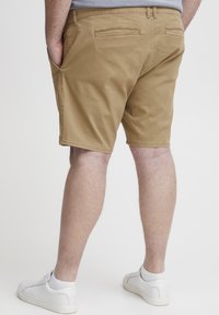 Khaki-Shorts mit entspannter Passform, aus Baumwolle, mit Seitentaschen und aufgesetzten Gesäßtaschen, kombiniert mit weißen Sneakern.