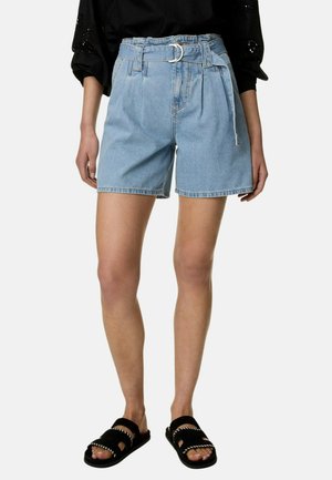 Personne portant un short en jean taille haute bleu clair avec une ceinture en tissu, un top noir et des sandales slides noires avec des coutures blanches.