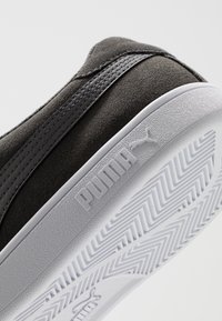 Sneaker in pregevole suede nero con suola in gomma bianca, caratterizzato da una superficie testurizzata e da un logo "PUMA" ben visibile sul lato.