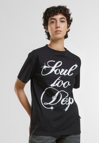 Camiseta de algodón negra de manga corta y cuello redondo, que presenta el texto estilizado en blanco "Soul too Deep" en el frontal.