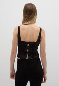 Top croppato in velluto nero con spalline larghe, retro con bottoni e tre fiocchi, e una finitura testurizzata.