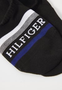 Black ankle socks featuring a horizontal stripe pattern in white and blue, with "HILFIGER" prominently displayed in white text.
