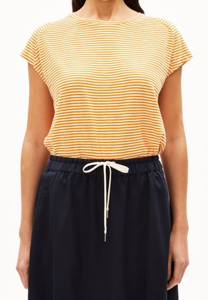 Woman wearing a yellow and white striped short-sleeve shirt tucked into navy drawstring pants.