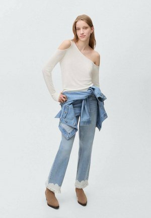 Ljusbeige, enaxlad tröja med långa ärmar, tillsammans med ljusblå denimjeans med fransar vid fållen. Bruna anklarstövlar fulländar looken.