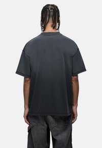 T-shirt nera in cotone oversize con maniche corte, colletto girocollo e un effetto sfumato da scuro a chiaro, texture liscia e cuciture minime.