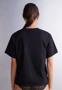 Černé bavlněné tričko s krátkým rukávem, klasickým výstřihem a uvolněným střihem. Hladká textura, minimální švy a jednoduchý design.