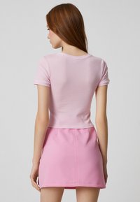 Top de manga corta de color rosa claro y con canalé, con un escote redondo, combinado con una falda corta rosa clara. Textura suave y diseño ajustado.