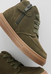 Olijfgroene suède hoge sneakers met een gestructureerde afwerking, voorzien van een zwarte rits en groene veters, gecombineerd met een lichtbruine rubberen zool.