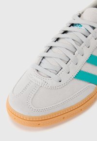 Grå ruskinds sneakers med turkise tre-striber, snørelukning og en tekstureret gummisål. Glat overflade.
