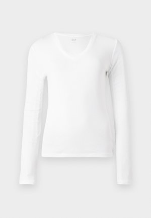Chemise blanche à manches longues, col en V, ajustée, présentée à plat sur un fond blanc.