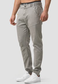 Graue Stretchhosen mit einem taillierten Design, ausgestattet mit genähten Paneeldetails, schrägen Fronttaschen und einem schwarzen Markenbund.