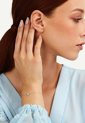Silver bracelet with a small round accent, worn on a hand. Light blue blouse with textured sleeves. Naturally styled hair.