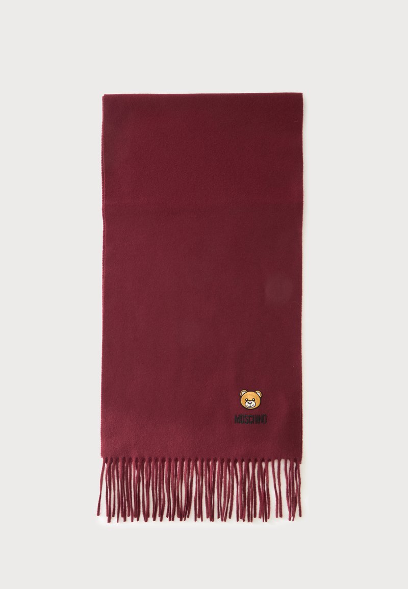Écharpe bordeaux à franges ornée d’un petit ours en peluche brodé et du logo Moschino près d’un coin.