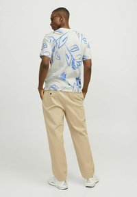 Kortärmad, ljusgrå t-shirt med blå blommönster, kombinerad med beige byxor, som visar en avslappnad passform och en mjuk tygtextur.