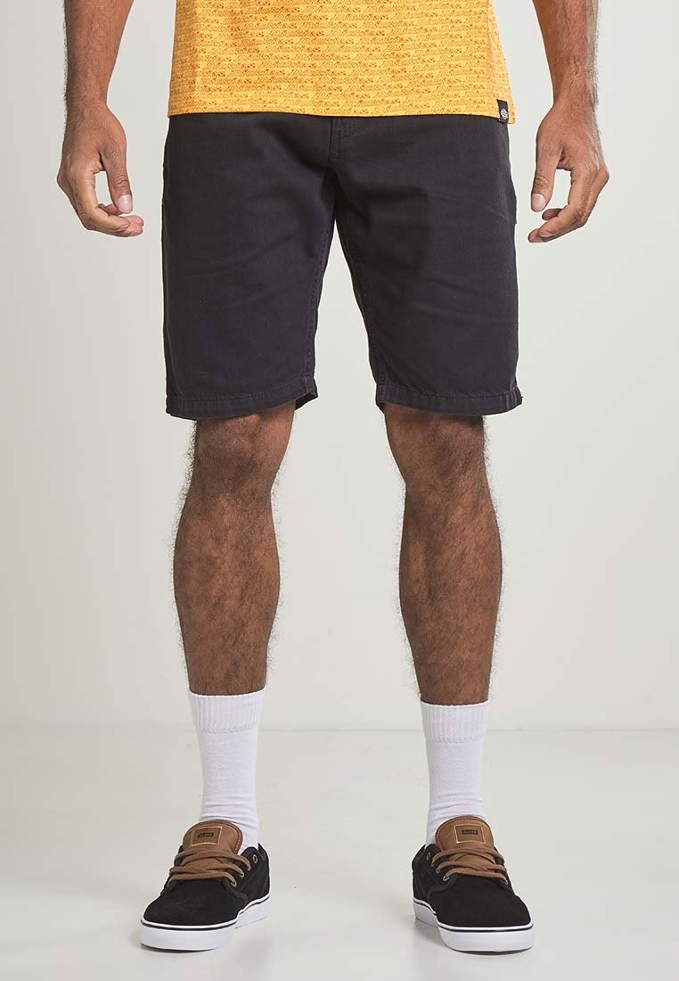 Black denim shorts with rolled cuffs, paired with white crew socks and black sneakers featuring brown accents. Model shown from waist down.