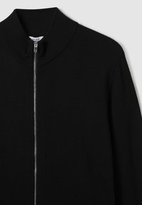 Maglione zip-up nero con colletto alto, realizzato in un tessuto a maglia testurizzato. Presenta una cerniera argentata e un design pulito e minimalista.