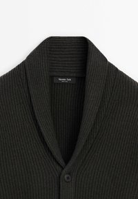 Cardigan gris foncé côtelé avec un col châle, doté d'une fermeture à un bouton et d'une étiquette de marque à l'intérieur. Tissu tricoté texturé.