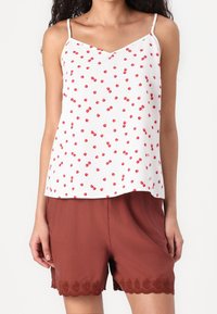 Débardeur blanc avec imprimé cerises rouges, bretelles fines et décolleté en V. Associé à un short marron avec un ourlet en dentelle festonnée.