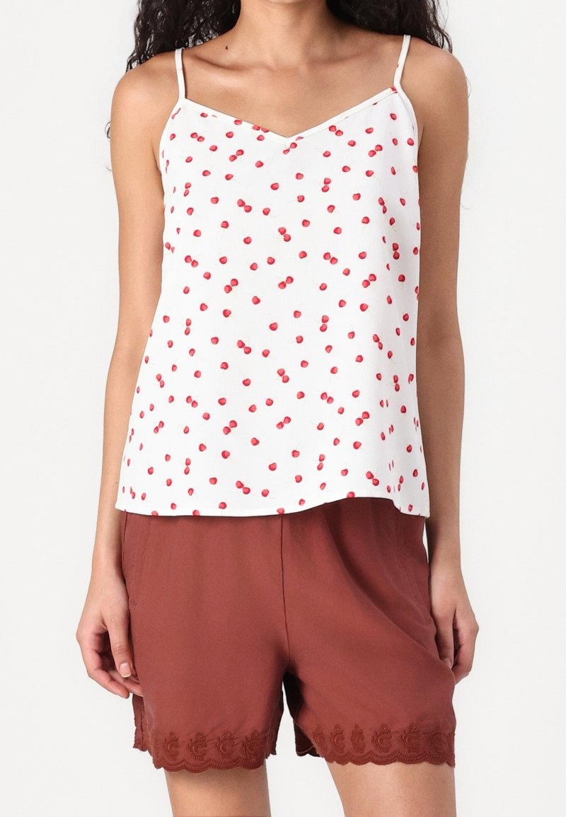 Débardeur blanc avec imprimé cerises rouges, bretelles fines et décolleté en V. Associé à un short marron avec un ourlet en dentelle festonnée.