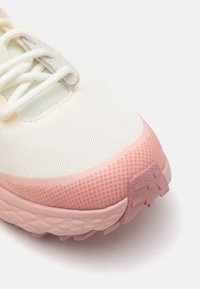 Lichte hardloopschoen met een witte mesh bovenkant, roze gradient tussenzool, getextureerde accenten en lichtgrijze veters. Ontworpen voor comfort en grip.