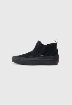 Basket montante Vans noire à enfiler avec dessus en daim, panneaux latéraux élastiques, languette au talon et semelle en caoutchouc sur fond gris clair uni.