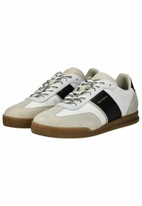 Tenisky s horní částí z kombinovaných materiálů, včetně bílé kůže, béžového semiše a černého pruhu. Klasický šněrovací design s texturovanou gumovou podrážkou.