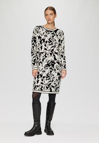 Abito in maglia con base nera, motivi floreali bianchi e azzurri chiari. Maniche lunghe, scollatura rotonda, forma aderente al corpo, abbinato a stivali neri al ginocchio.