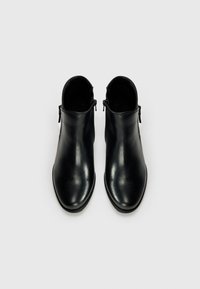 Två eleganta svarta ankelboots med en slät yta, med blixtlås på sidorna, placerade på en vit bakgrund.