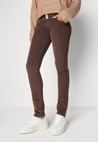 Hnědé kordové skinny džíny s vertikálním žebrováním, s dvoupanelovým zapínáním, předními kapsami a v kombinaci s bíl�ými teniskami.