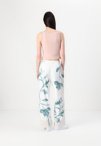 Light pink ribbed tank top paired with white wide-leg trousers featuring teal floral prints. Simple design with elastic waistband and white shoes.
