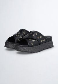 Chanclas de plataforma negras con amplias correas entrelazadas adornadas con pequeños patrones de eslabones de cadena plateados y suelas texturizadas brillantes.
