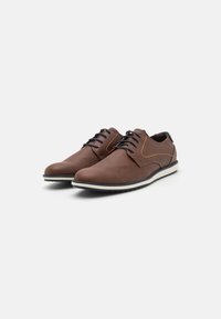 Zapatos marrones de cordones hechos de cuero texturizado, con costuras naranjas, suela de goma blanca y un diseño aerodinámico.
