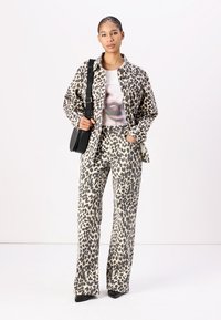 Giacca camicia con stampa leopardata e pantaloni a campana coordinati, realizzati in un materiale morbido e testurizzato, abbinati a una maglietta grafica e una borsa nera.