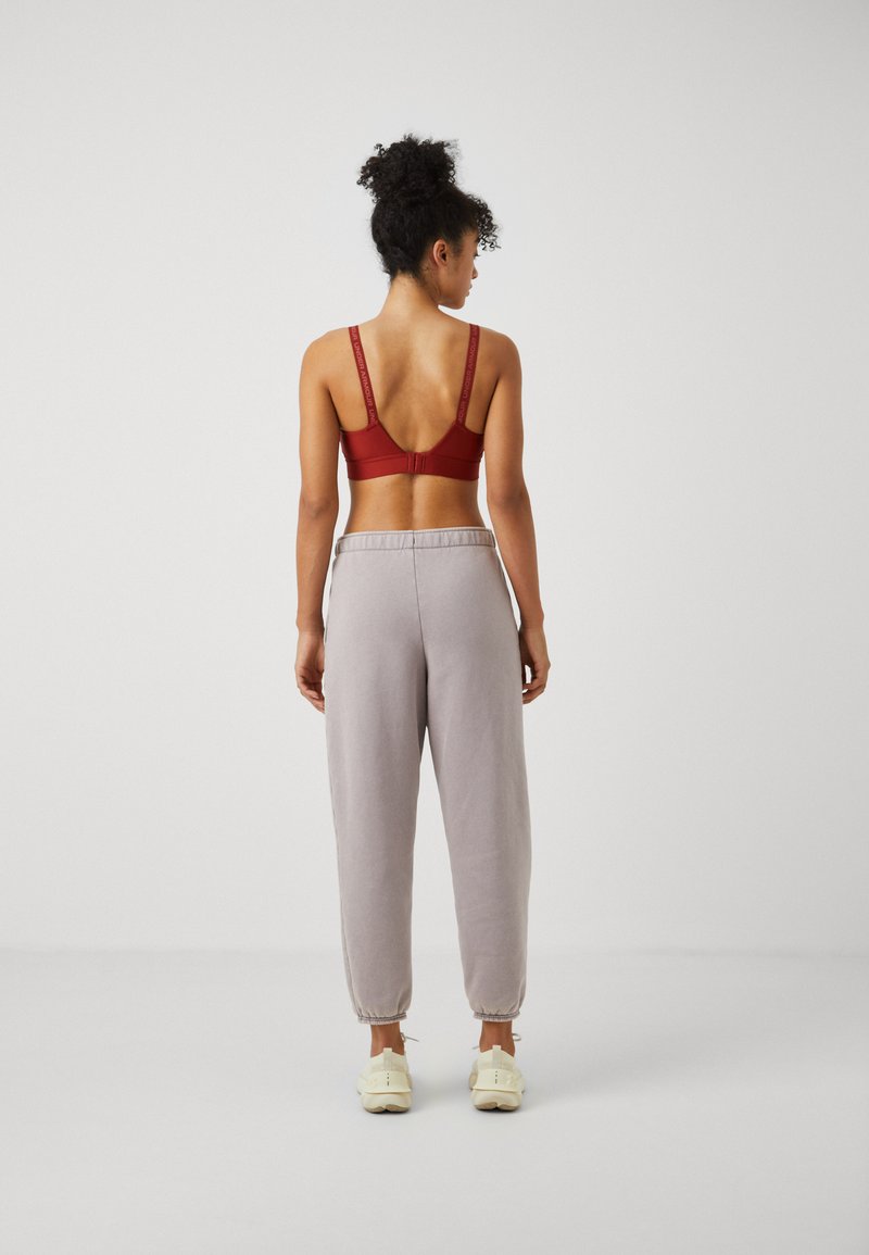 Rote Sport-BH mit verstellbaren Trägern, kombiniert mit hellgrauen Jogginghosen mit elastischen Bündchen und lockerer Passform. Weiße Sneaker runden den Look ab.