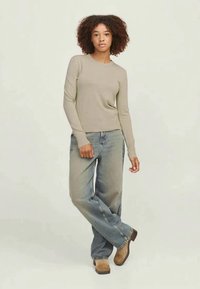 Top de malha de manga longa em bege, emparelhado com jeans soltos de lavagem clara e botas de cano curto castanhas. Ajuste casual com decote canelado e tecido texturizado.