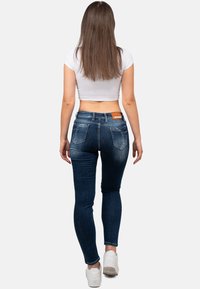Jeans skinny blu scuro a vita alta, con una leggera scoloritura, due tasche posteriori e un'etichetta in pelle in vita.