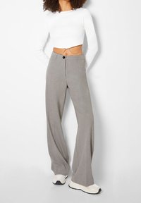 Grijze wijde broek met een gladde textuur, hoge taille en knoopsluiting, gecombineerd met een cropped witte top met lange mouwen.