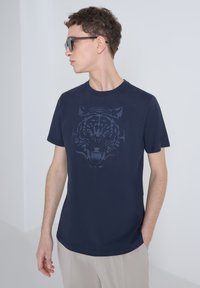 Camiseta de algodón azul marino con un gran gráfico de un tigre oscuro en la parte frontal. Diseño de mangas cortas y cuello redondo. Textura suave.