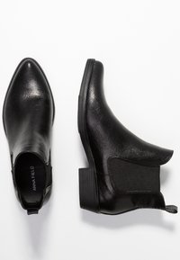 Bottines noires arrivant à la cheville avec un bout pointu, en cuir synthétique texturé. Dotées de panneaux élastiques sur les côtés et d'un petit talon carré.