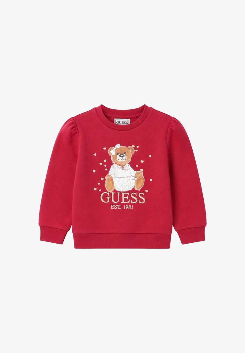 Sweat-shirt rouge pour enfants avec un ours en peluche portant une robe blanche et un nœud, entouré de petits cœurs, et texte "GUESS EST. 1981" en dessous.