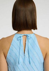 Abito senza maniche blu chiaro con strisce diagonali sfrangiate, caratterizzato da un'apertura a occhiello sul retro legata con un nastro. Tessuto liscio.