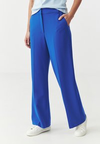 Wide-leg trousers in bright blue fabric, featuring a flat waistband, side pockets, and smooth texture; paired with white sneakers.