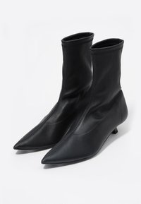 Czarne botki za kostkę o gładkiej, gładkiej powierzchni, spiczastych noskach i dopasowanym trzewiku. Wykonane z miękkiego materiału o minimalistycznym designie. Płaskie obcasy.