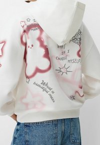 Felpa bianca con design spray-paint rosa e grigio, che include stelle, nuvole e testo scritto a mano. Tessuto morbido con una vestibilità rilassata.