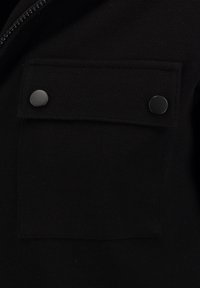 Chaqueta negra con tejido texturizado, un bolsillo en el pecho con solapa y dos botones a presión negros para un cierre seguro.
