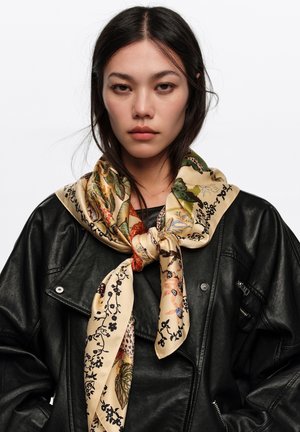 Młoda kobieta o prostych ciemnych włosach, ubrana w czarną skórzaną kurtkę i przewiązany wokół szyi jedwabny beżowy szalik w kwiaty.