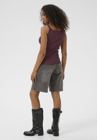 Débardeur bordeaux, shorts en denim gris et bottes noires montantes avec des boucles. Le débardeur a une coupe ajustée et les shorts sont de longueur genou.