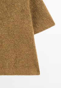 Gros plan sur un tissu en laine brune et duveteuse avec une couture ou un pli visible sur un fond blanc.