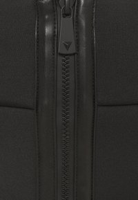 Zwarte ritssluiting kledingstuk met een gladde textuur, voorzien van een hexagonale ritshendel en strakke stoffenpanelen aan weerszijden van de rits.